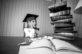 Smart girl in graduation cap looking at high heap of books