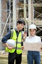 Smart asian male engineer and female architect in the construction site, checking the blueprint together Royalty Free Stock Photo