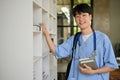 A smart Asian male medical student in scrubs choosing a book on the shelf in the library Royalty Free Stock Photo