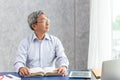 Smart healthy business old man sitting in office, Asian elder thinks looking out of the windows while reading a book Royalty Free Stock Photo