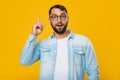 Smart inspired adult european male with beard in glasses raises finger up, isolated on yellow background