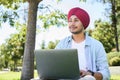 Smart inspired male Indian entrepreneur wearing red traditional headwrap turban pheta using laptop