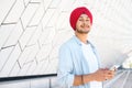 Smart inspired male Indian entrepreneur wearing red traditional headwrap turban pagg using smartphone