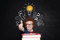 Smart kid holding book and showing thumb up against lightbulb on chalkboard background. Brainstorming and idea concept Royalty Free Stock Photo