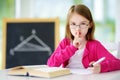 Smart little schoolgirl with pen and books writing a test in a classroom Royalty Free Stock Photo