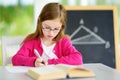 Smart little schoolgirl with pen and books writing a test in a classroom. Child in an elementary school. Royalty Free Stock Photo