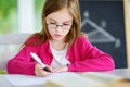 Smart little schoolgirl with pen and books writing a test in a classroom. Child in an elementary school. Royalty Free Stock Photo