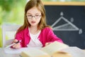 Smart little schoolgirl with pen and books writing a test in a classroom. Child in an elementary school. Royalty Free Stock Photo