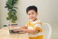 Smart looking Asian preteen boy writing and using computer laptop studying online lessons