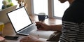 A smart man is taking notes while sitting in front of a white blank screen computer laptop that putting on a wooden working desk. Royalty Free Stock Photo