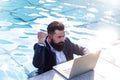 Smart man using a laptop near the pool. Business man in suit with notebook on swimming pool. Funny businessman with