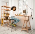 Smart millennial working laptop at home sitting near window. Arabic freelancer in white shirt and jeans smiles looking