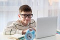 Smart nerd kid boy in glasses behind ear sitting at his desk at home using a laptop computer Royalty Free Stock Photo