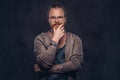 Smart pensive redhead hipster with full beard and glasses dressed in casual clothes, poses with hand on chin in a studio