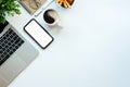 Smart phone with blank screen, laptop computer, coffee cup and stationery on white office desk. Top view Royalty Free Stock Photo