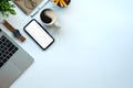 Smart phone with blank screen, laptop computer, coffee cup and stationery on white office desk. Top view Royalty Free Stock Photo