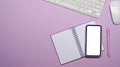 Smart phone with empty screen, notebook and wireless keyboard on purple background. Royalty Free Stock Photo