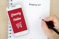 Smart phone with grocery online on screen and shopping list back Royalty Free Stock Photo