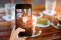 Smart phone in hand with latte coffee and cake on table. Royalty Free Stock Photo