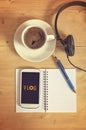 Smart phone with headset, notebook, pencil, coffe cup on wooden table.