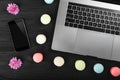 Smart phone, notebook computer and macarons with flowers on black wooden table, top view Royalty Free Stock Photo