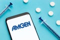 Smart phone showing Amgen logo on screen and pills and syringe on blue background