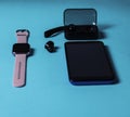 Smart phone, a smart watch with a pink band, a wireless earphones case on a neon blue background Royalty Free Stock Photo