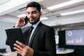 Smart and positive businessman call and talk on a smartphone alone while watching a digital tablet in the office. Royalty Free Stock Photo