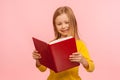 Smart positive cute little girl reading big red book and smiling happily, learning homework, being curious