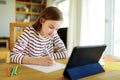 Smart preteen schoolgirl doing her homework with digital tablet at home. Education and distance learning for kids. Homeschooling Royalty Free Stock Photo