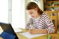 Smart preteen schoolgirl doing her homework with digital tablet at home. Education and distance learning for kids. Homeschooling Royalty Free Stock Photo
