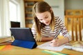 Smart preteen schoolgirl doing her homework with digital tablet at home. Education and distance learning for kids. Homeschooling