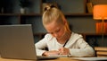 Smart pretty primary schoolgirl blonde little pupil seven years old kid studying in house room writing homework doing