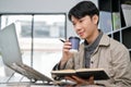 Smart Asian male programmer or web developer sipping coffee and using laptop computer Royalty Free Stock Photo