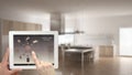 Smart remote home control system on a digital tablet. Device with app icons. Blurry interior of minimalist kitchen in the backgrou Royalty Free Stock Photo