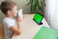 smart school boy siting at desk and looks at tablet. Happy child showing his picture