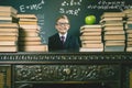 Smart school boy sitting at table with many books