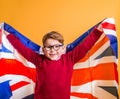 Smart school kid boy holding the UK flag on yellow wall background. Learn English concept. Summer education camp Royalty Free Stock Photo