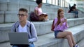 Smart school pupil eyeglasses holding laptop sitting outdoors, college education