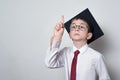 Smart schoolboy in academic hat raised index finger up. Graduating little student kid