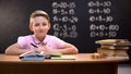 Smart schoolboy smiling to camera after solving task, exercises written behind