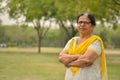 Smart senior north Indian woman standing, posing for the camera with hands crossed in a park wearing yellow salwar kameez in Royalty Free Stock Photo