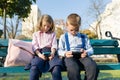 Smart serious children boy and girl are looking into smartphones. On a bench with school backpacks