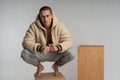 Smart serious young man in sportwear crouched on wood cube and posing Royalty Free Stock Photo