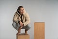 Smart serious young man in sportwear crouched on wood cube and posing Royalty Free Stock Photo