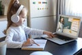 Smart small preschooler girl in headphones watch online lesson and communicate with teacher at home