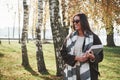 Smart student on a walk. Young smiling brunette in sunglasses stands in the park near the trees and holds notepad Royalty Free Stock Photo