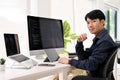 Smart Asian male web developer sits at his modern office desk, smiling and looking at the camera Royalty Free Stock Photo