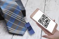 Hand holding smartphone with scanning QR code sign screen with necktie on white wooden backgroun