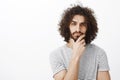 Smart thougtful attractive hispanic guy with beard and curly hair, holding hand on chin, thinking and focusing at camera